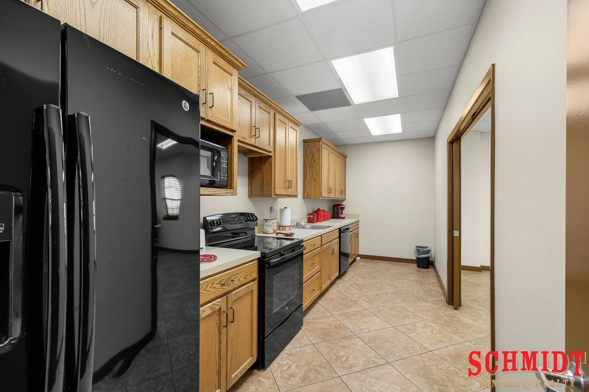 Warm wood cabinetry, black appliances, tile flooring, recessed lighting, and a drop ceiling