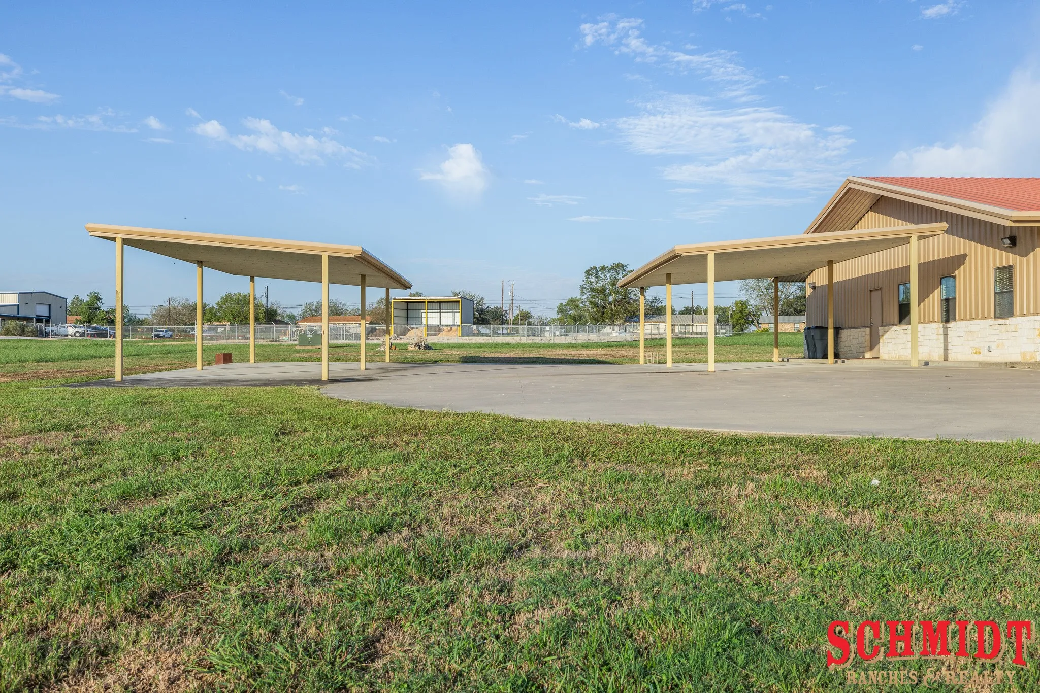 Two covered parking structures, paved drive, and a building with a red roof and stone base