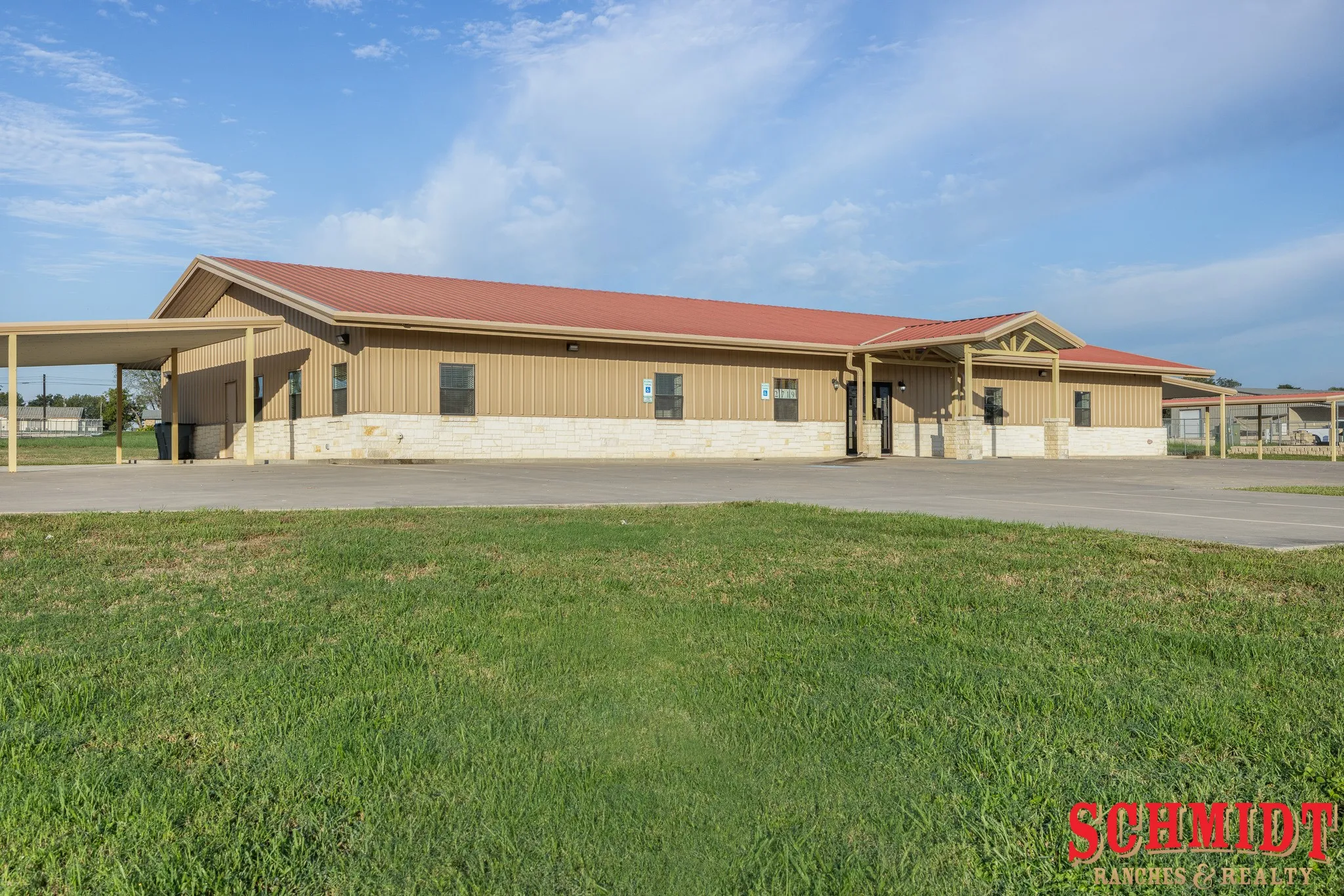 Metal building with a red roof, stone wainscoting, and multiple covered parking structures