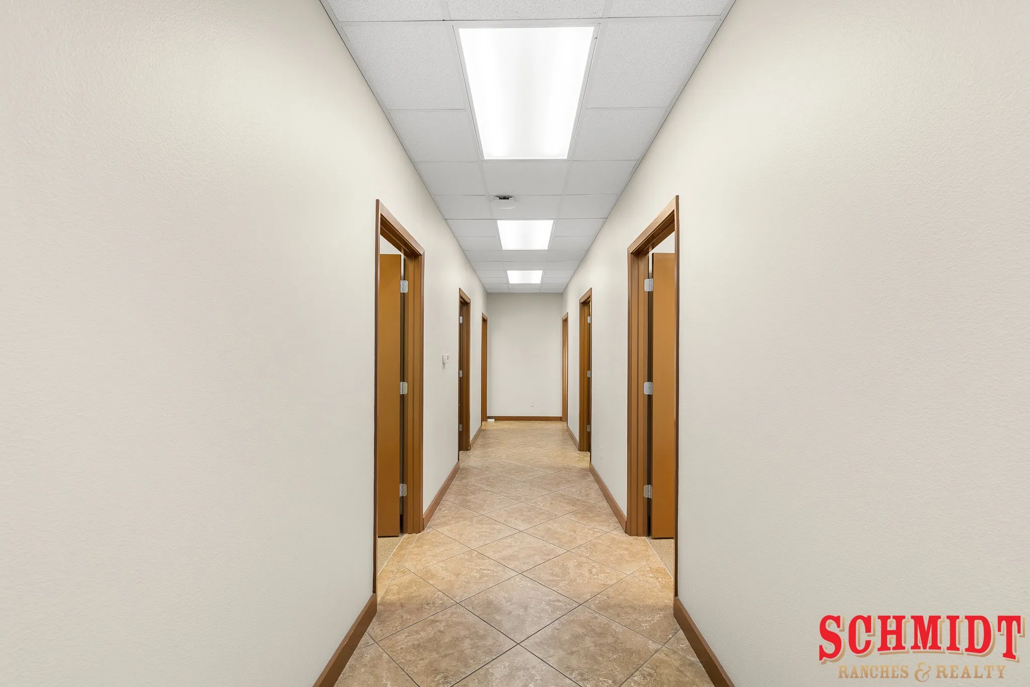 Hallway with neutral-toned walls, wood-finish door frames, and diagonal tile flooring