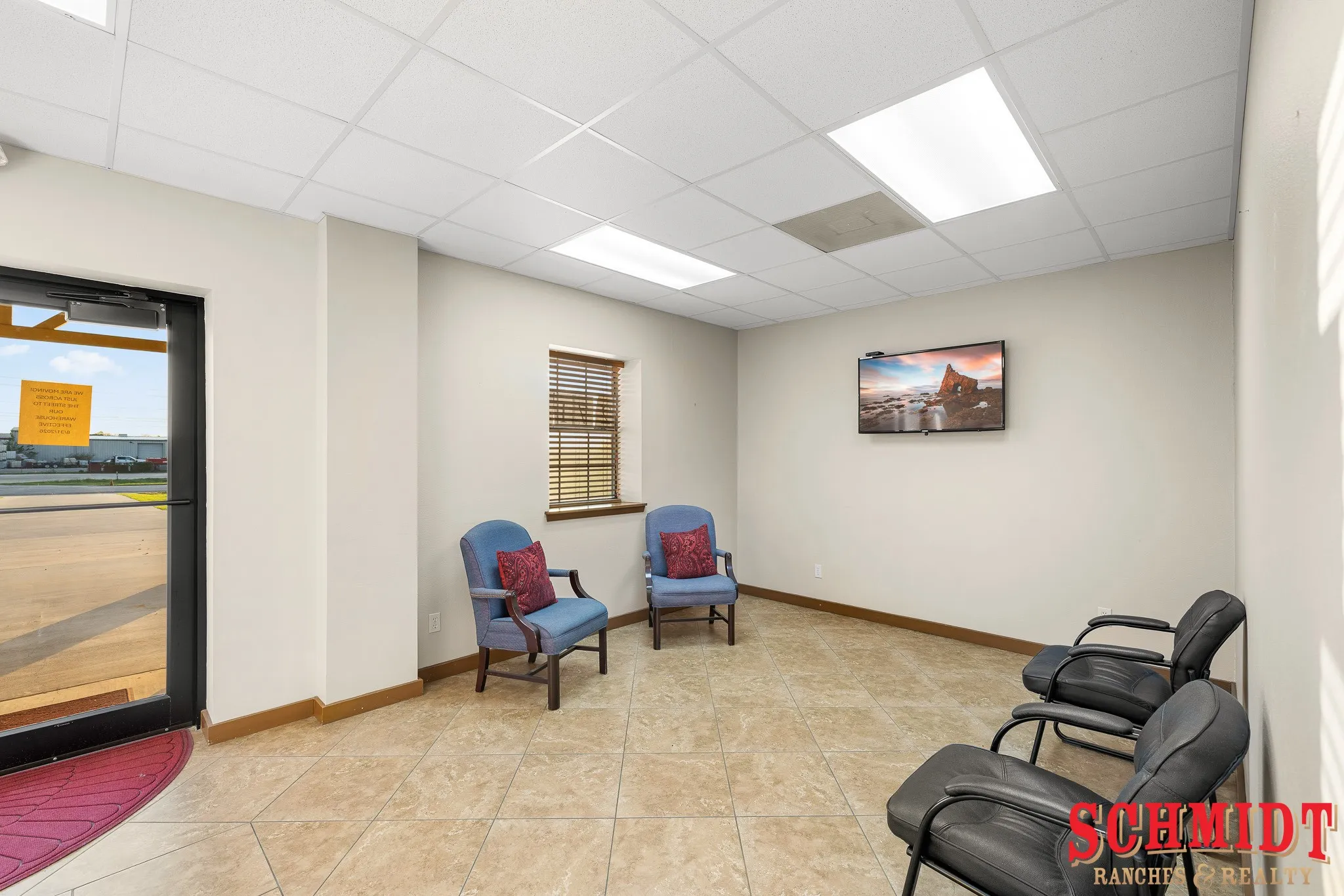 Tiled flooring, drop ceiling with integrated lighting, wood-finish blinds, and a wall-mounted display