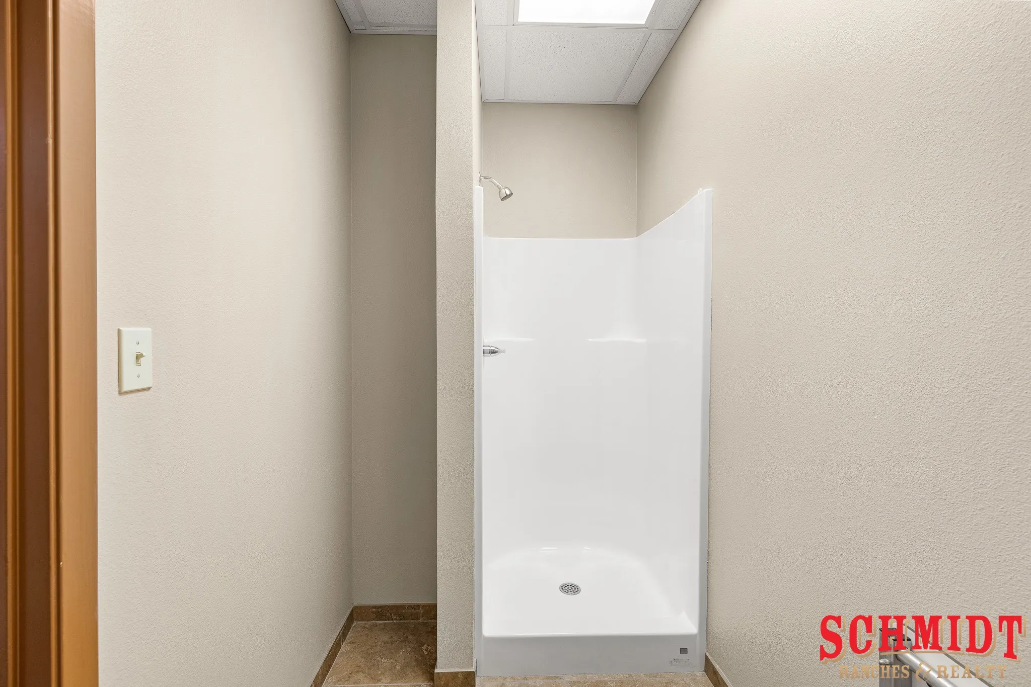 White shower stall with a chrome shower head, light-colored walls, and floor tiling