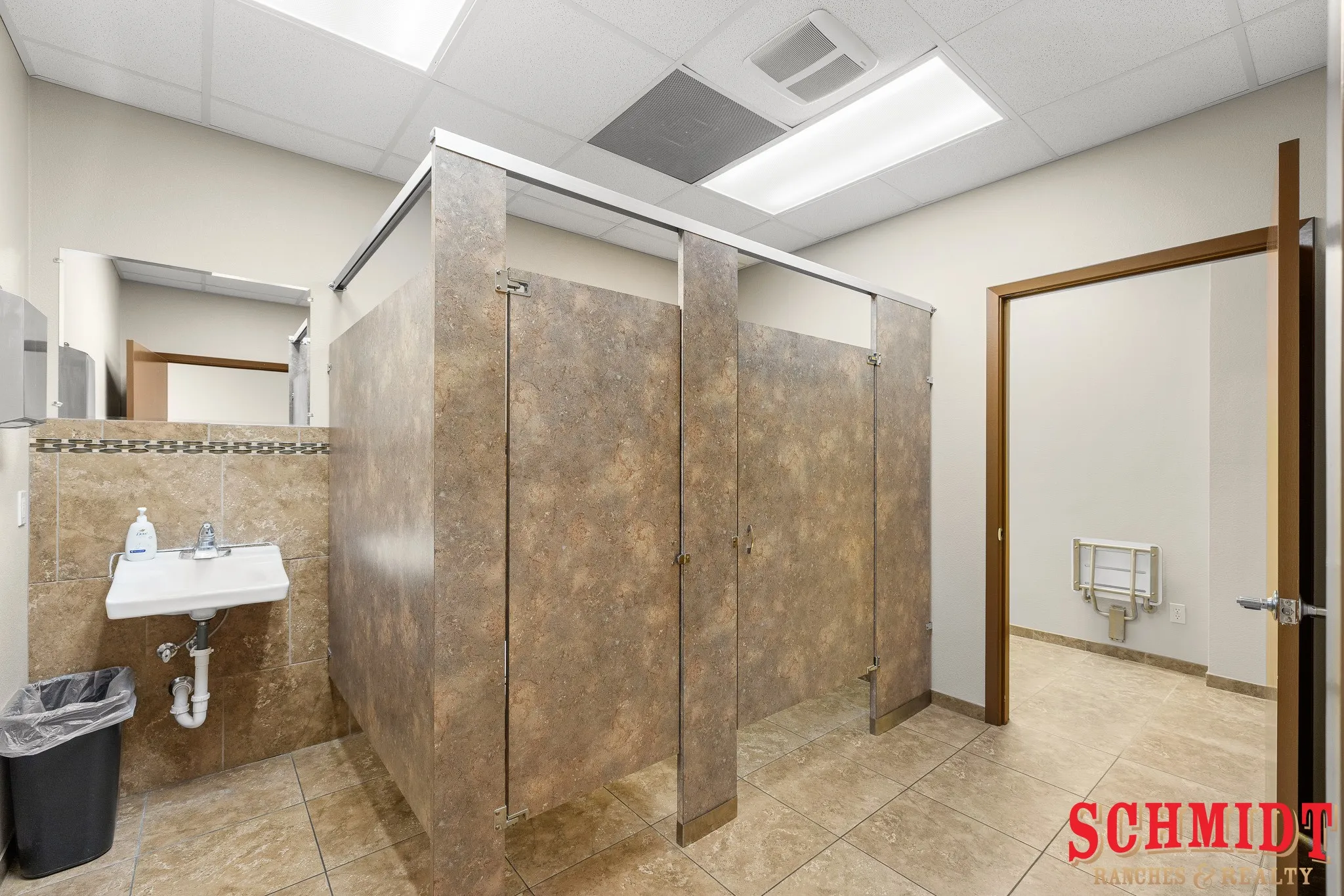 Tile flooring and wainscoting, individual stalls, and a wall-mounted sink with mirror