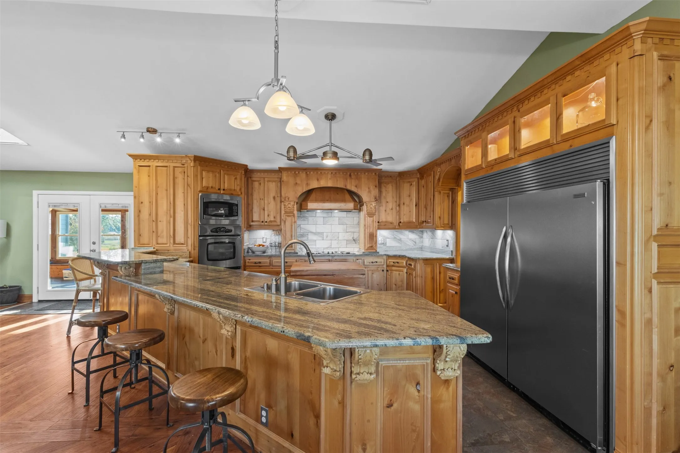 Kitchen featuring decorative light fixtures, backsplash, built in appliances, dark stone countertops, and a breakfast bar area