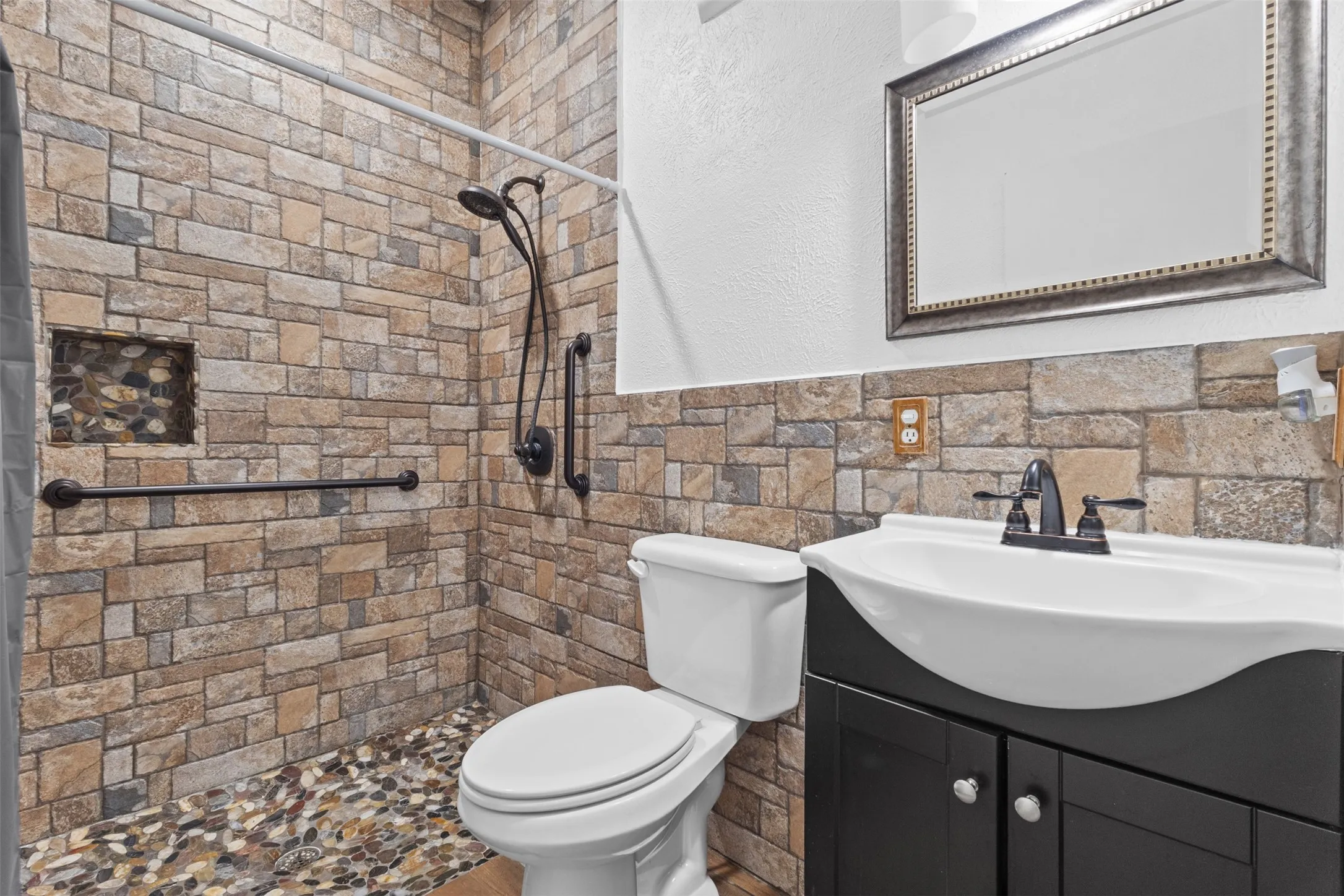 Full bathroom with vanity, a tile shower, a textured wall, tile walls, and wainscoting