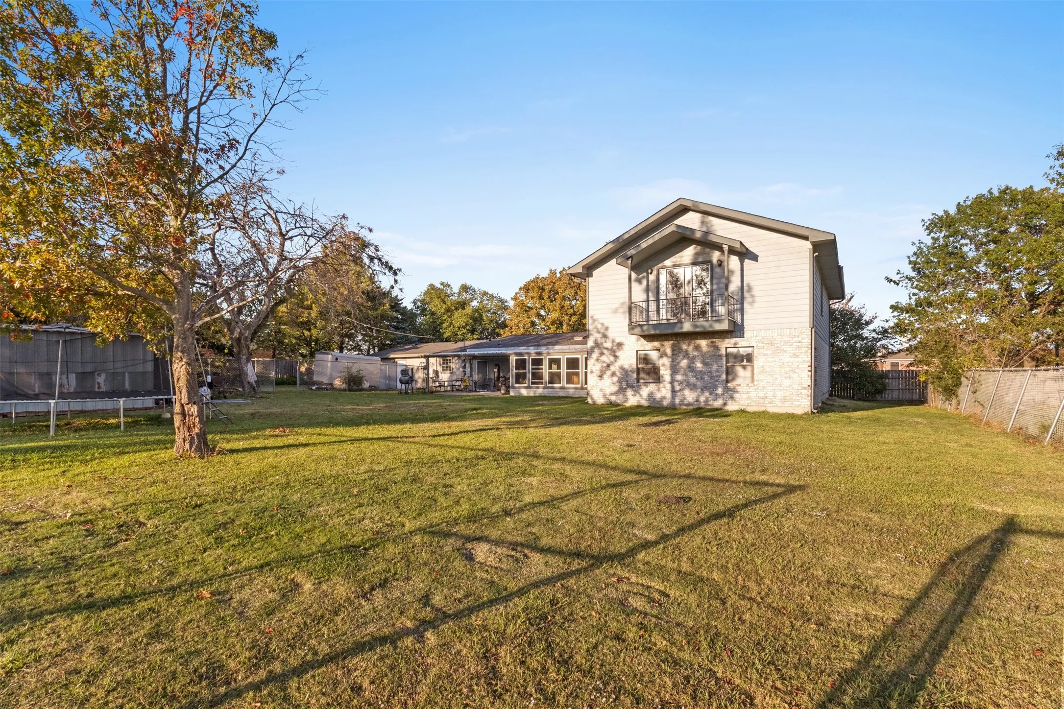 Back of house with a fenced backyard, a trampoline, and a balcony