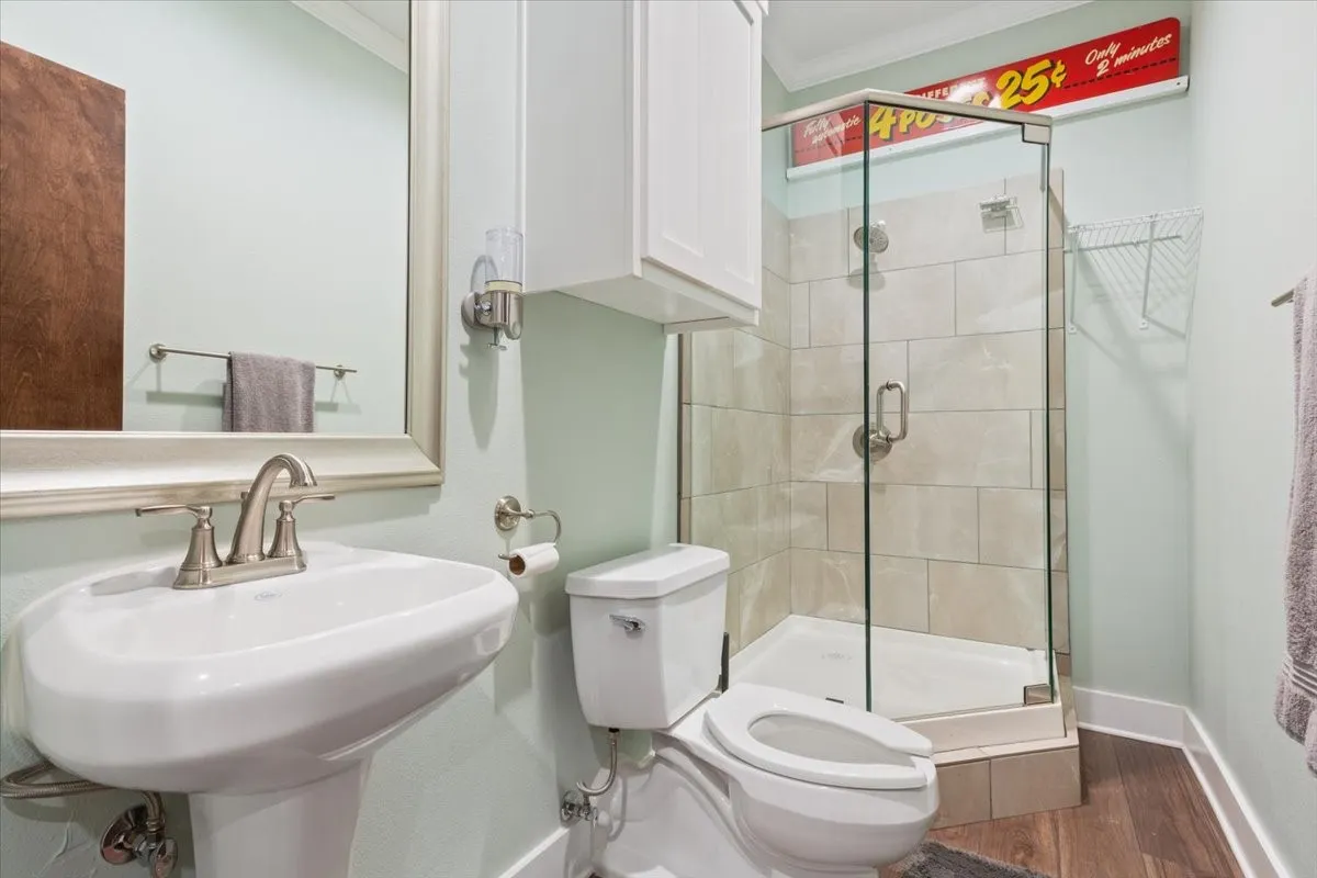 Full bathroom featuring dark wood-style floors, a stall shower, and crown molding