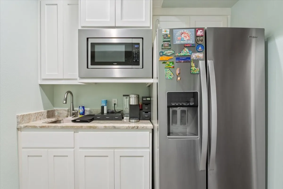 Kitchen with stainless steel refrigerator with ice dispenser, white cabinets, and light stone countertops