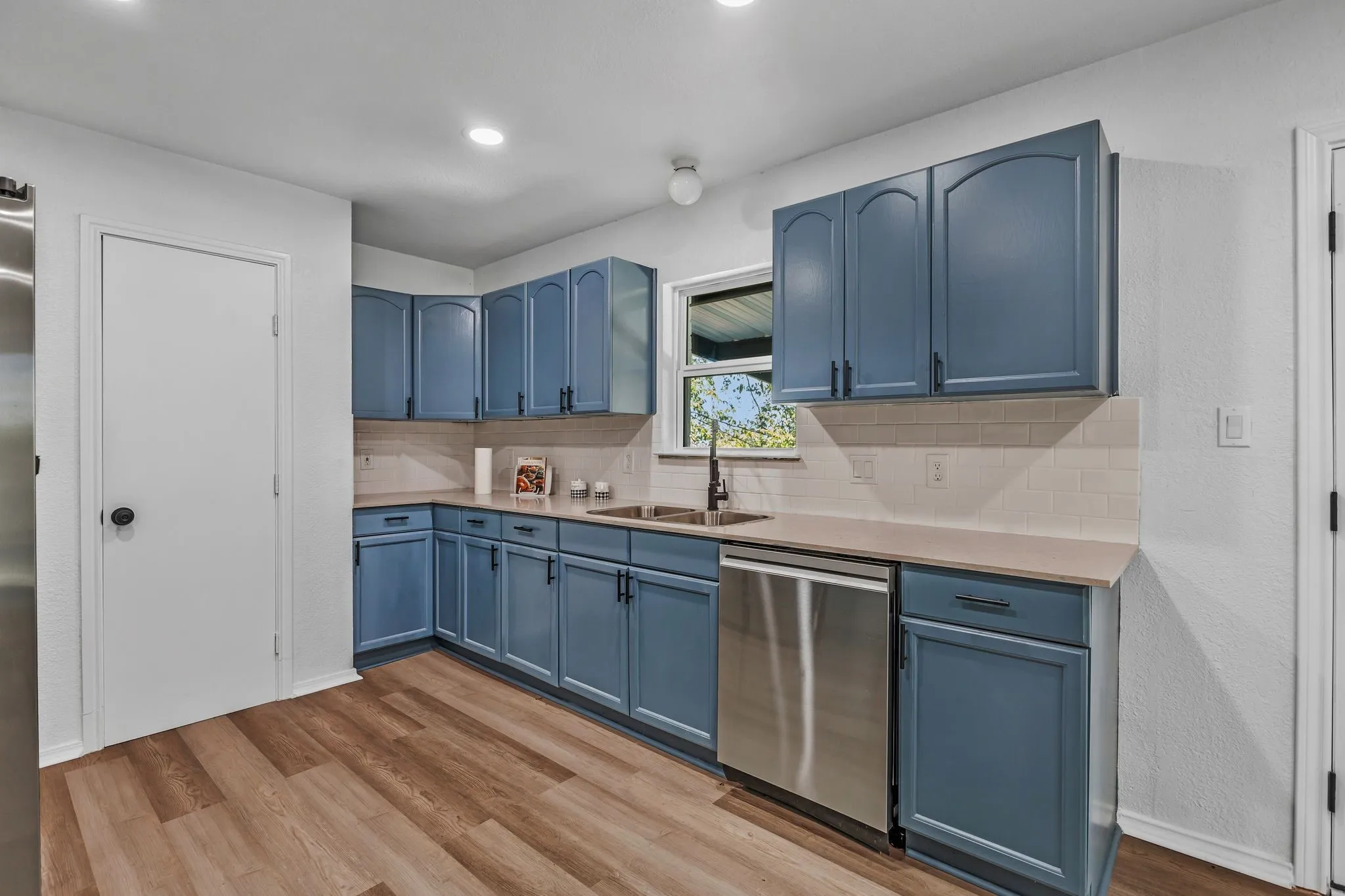 Kitchen featuring blue cabinetry, stainless steel appliances, light wood-style flooring, tasteful backsplash, and a textured wall