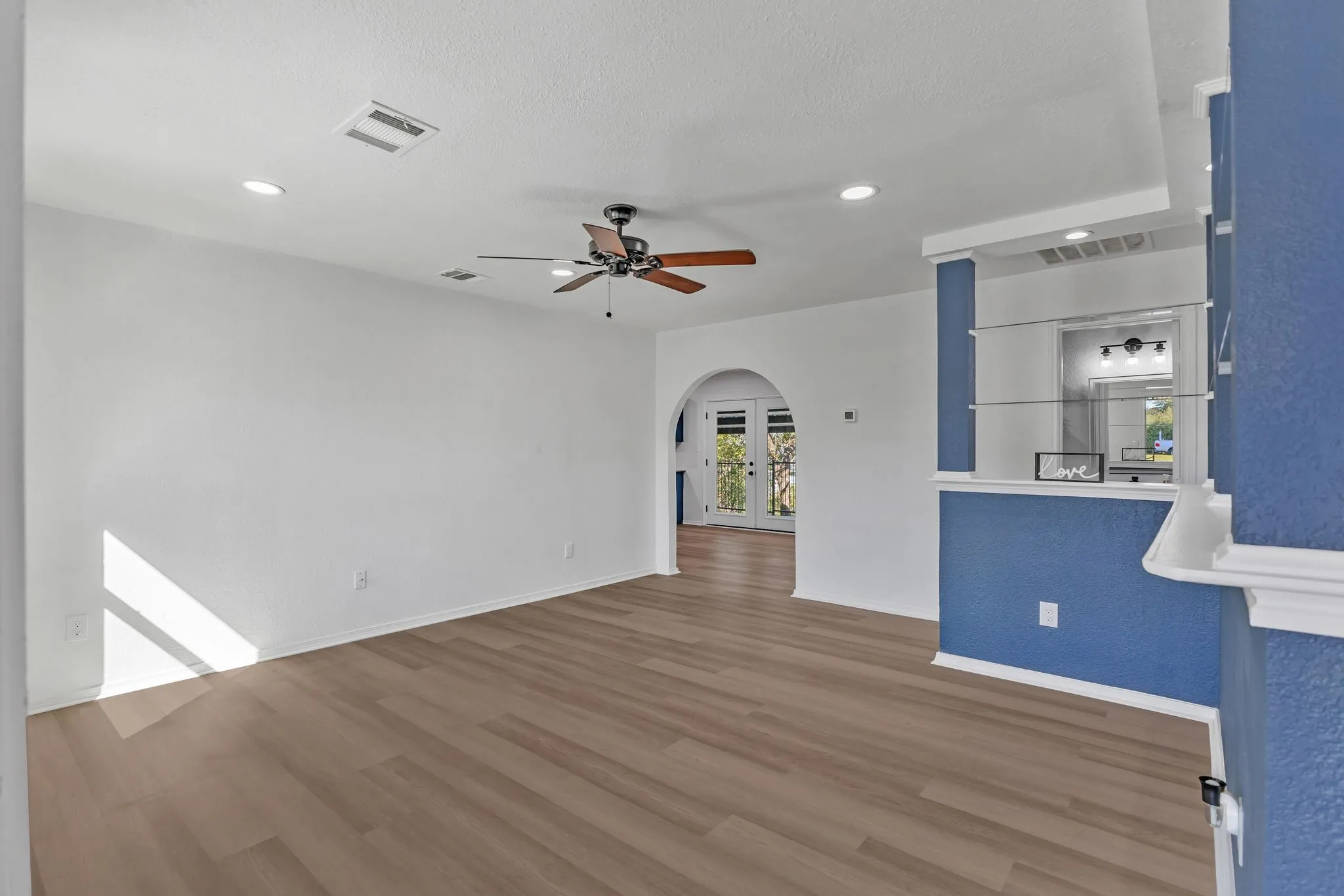 Unfurnished living room featuring arched walkways, wood finished floors, recessed lighting, ceiling fan, and french doors