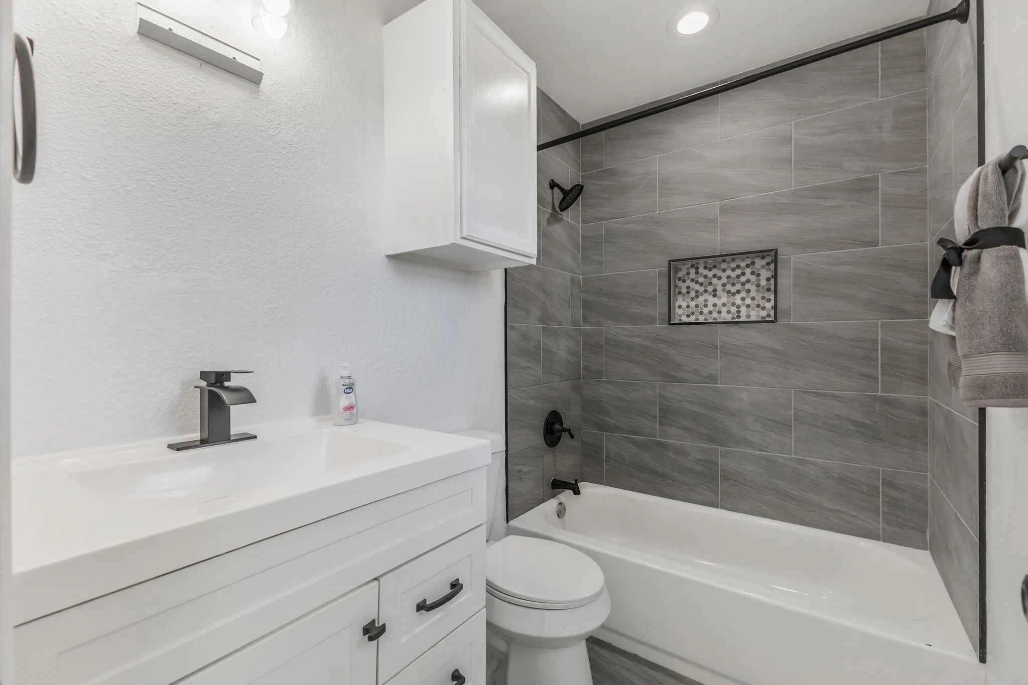 Bathroom with vanity, tub / shower combination, a textured wall, and recessed lighting