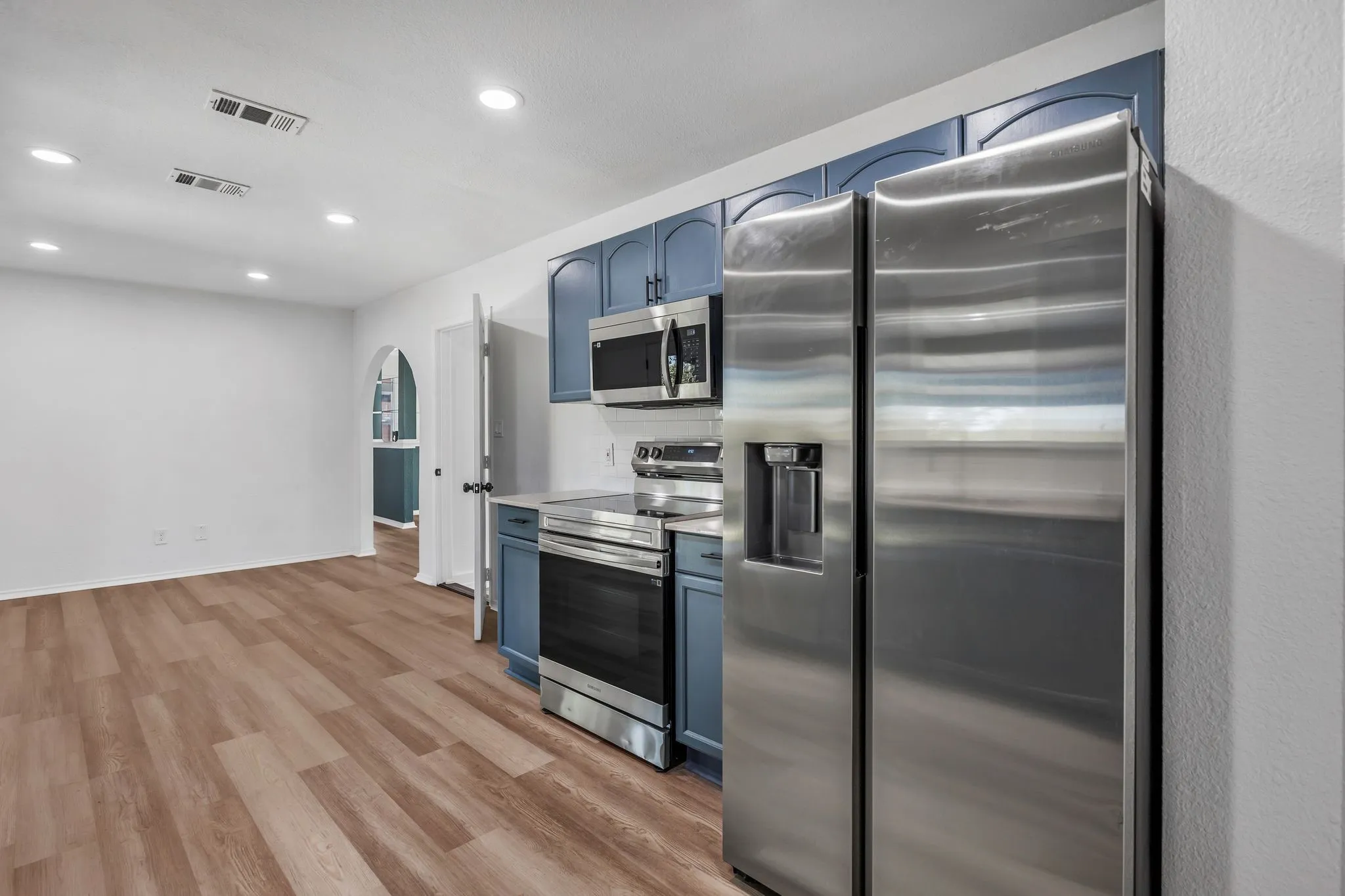 Kitchen featuring blue cabinets, appliances with stainless steel finishes, light countertops, arched walkways, and recessed lighting
