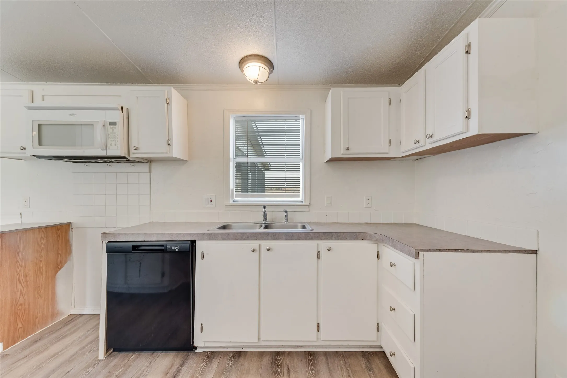 Kitchen featuring black dishwasher, white cabinetry, light wood-type flooring, white microwave, and light countertops