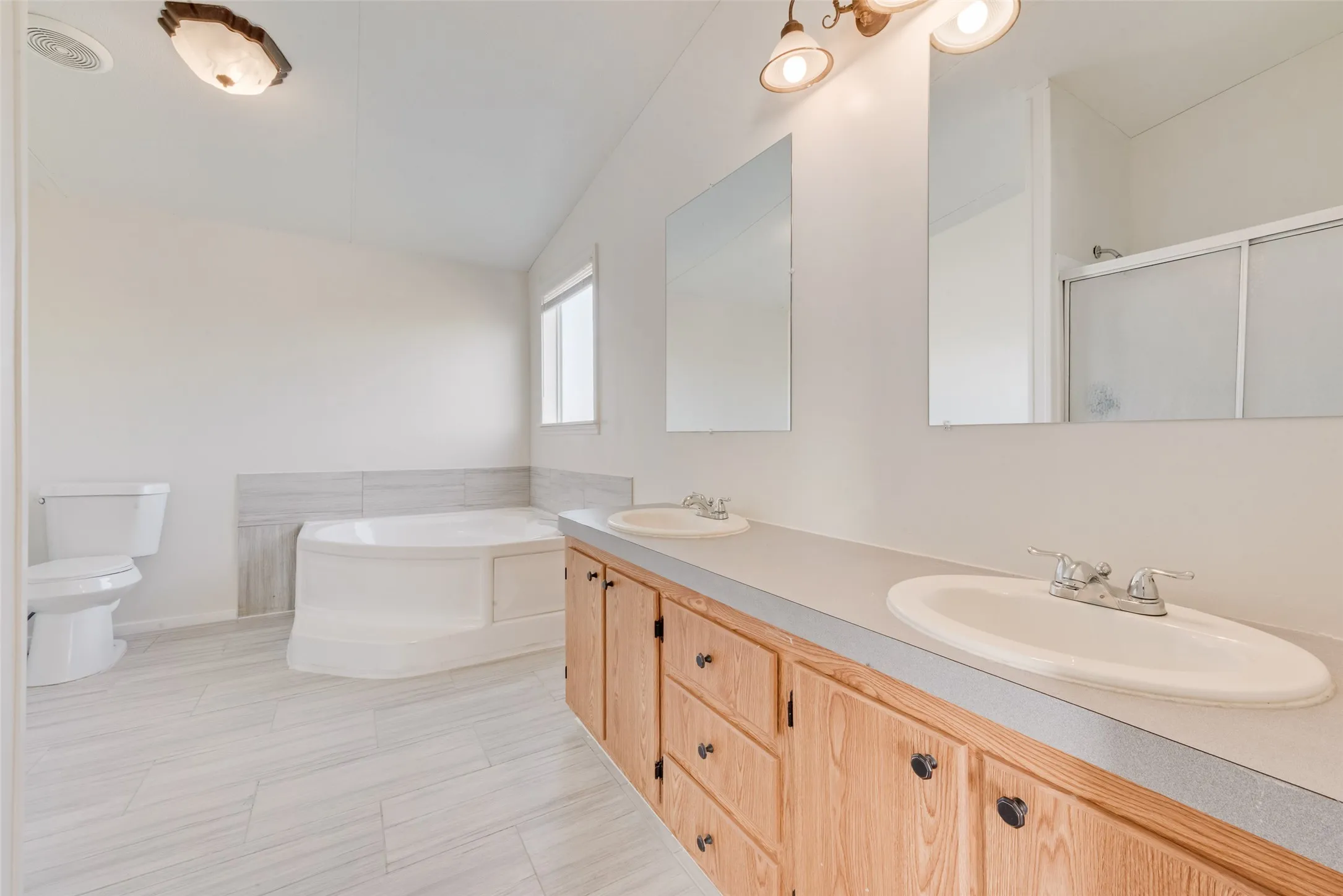 Bathroom featuring a bath, double vanity, a shower stall, and lofted ceiling