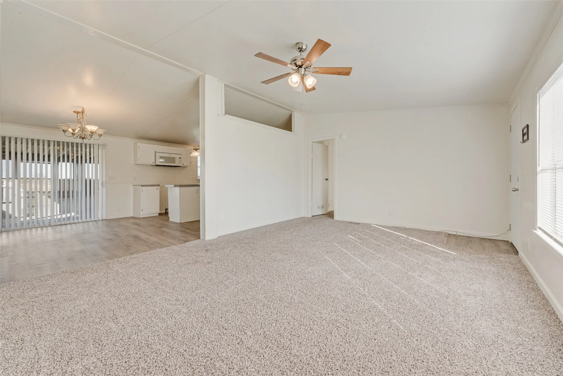 Unfurnished living room featuring light colored carpet, vaulted ceiling, a chandelier, and ceiling fan