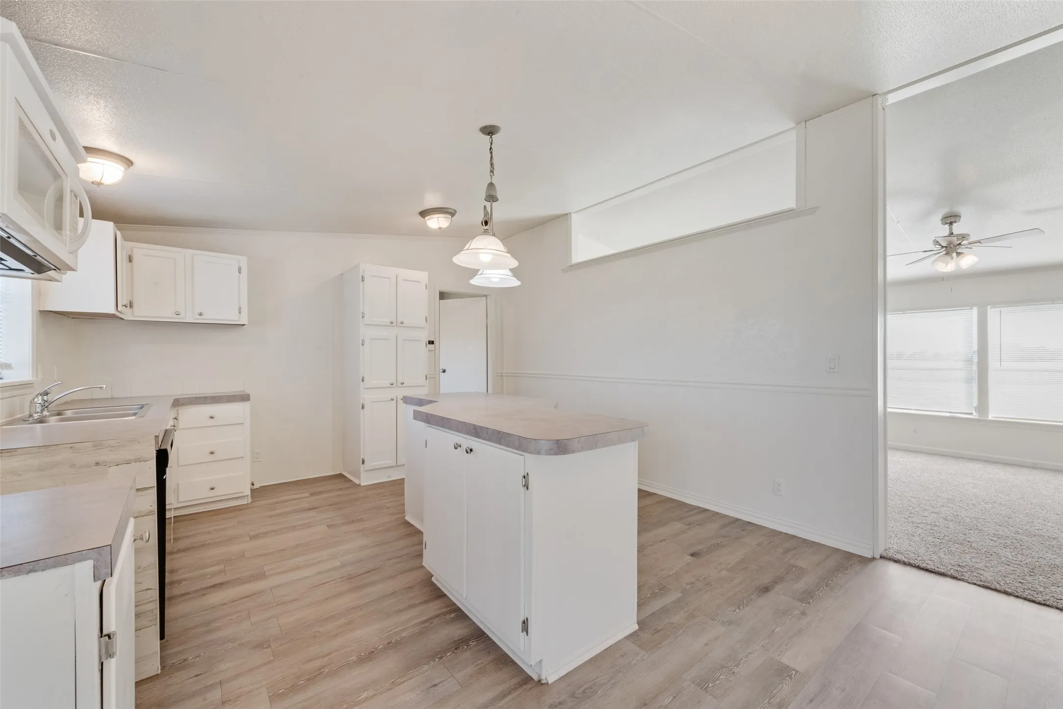 Kitchen featuring white cabinets, decorative light fixtures, a center island, white microwave, and light countertops