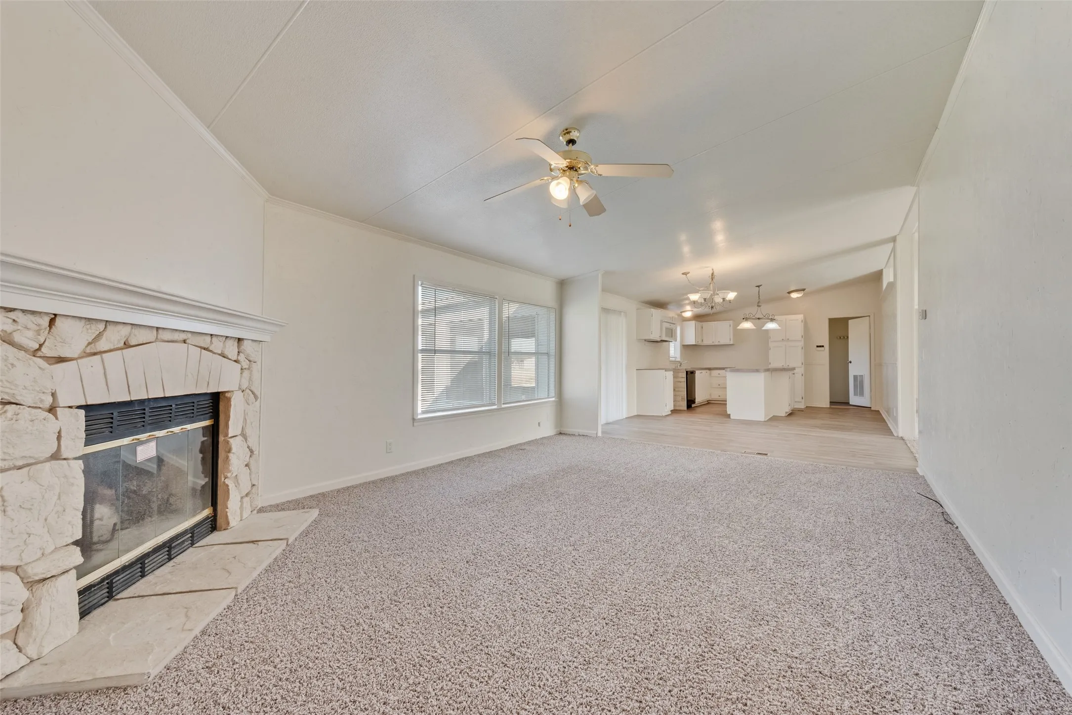 Unfurnished living room with light colored carpet, a fireplace, a ceiling fan, and a chandelier