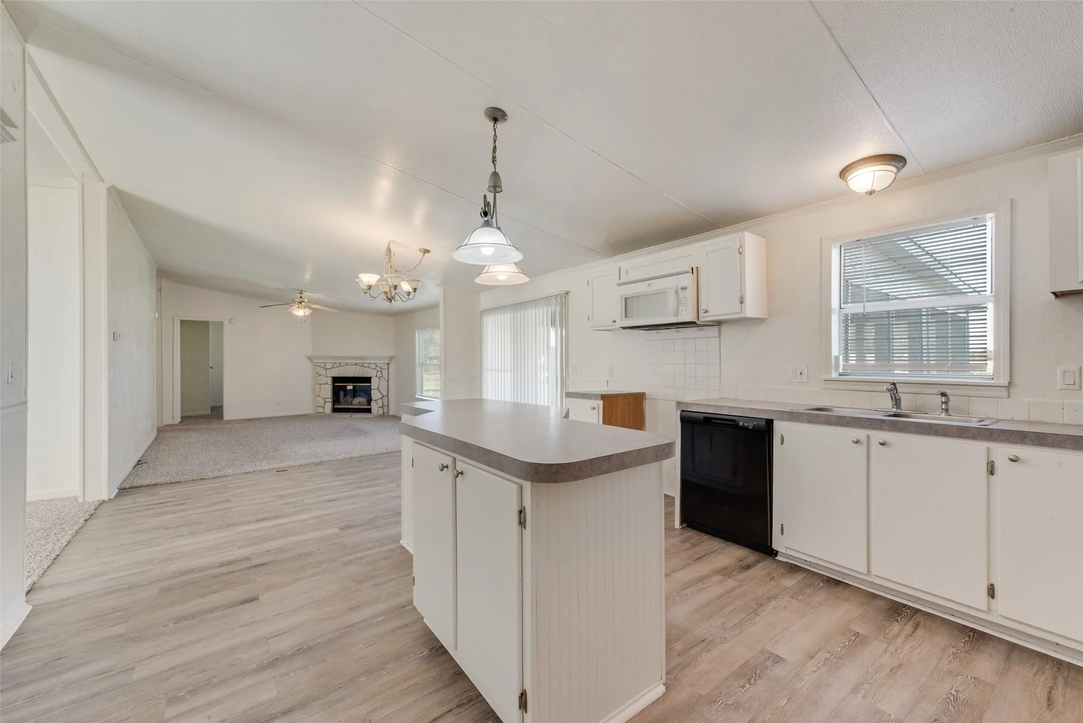 Kitchen featuring a glass covered fireplace, a kitchen island, white cabinetry, black dishwasher, and open floor plan