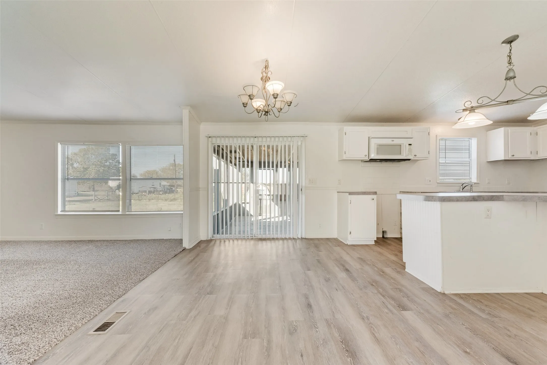 Kitchen featuring white cabinets, a chandelier, decorative light fixtures, white microwave, and light countertops