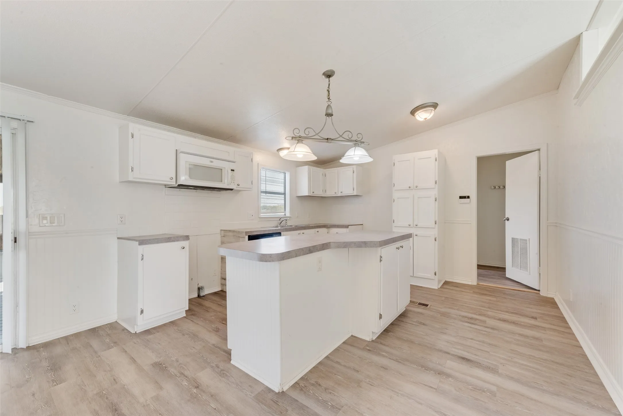 Kitchen featuring hanging light fixtures, white cabinetry, a center island, light wood-type flooring, and vaulted ceiling
