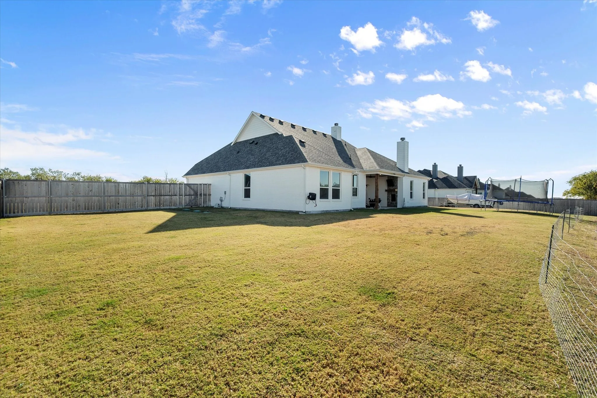Rear view of property with a fenced backyard, a chimney, a trampoline, a patio, and a shingled roof