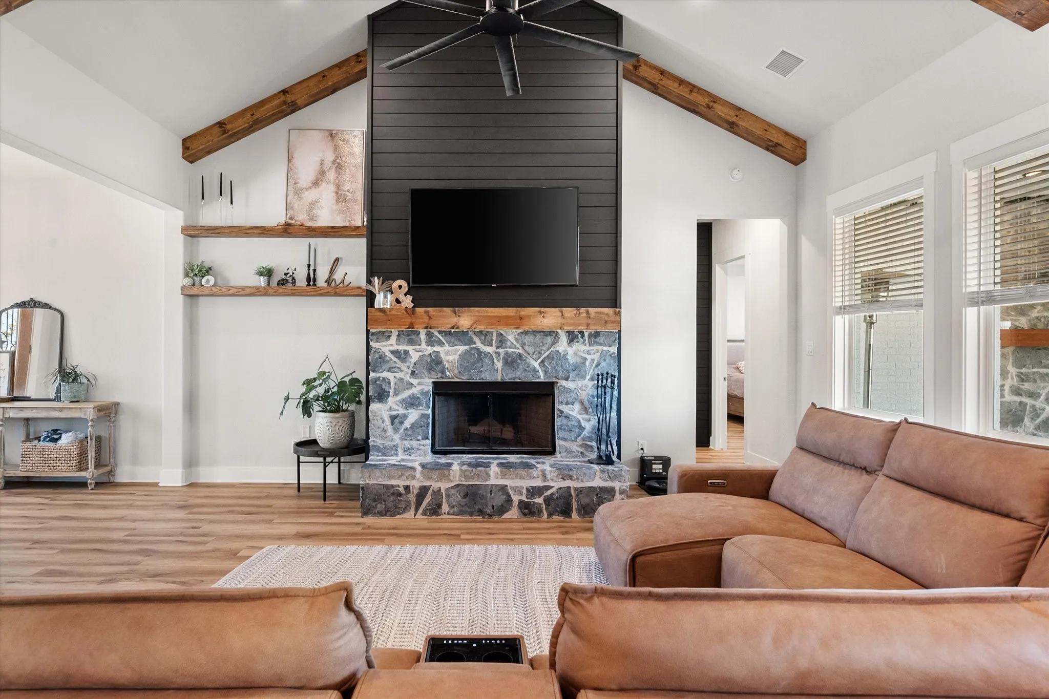 Living room with wood finished floors, a stone fireplace, and a ceiling fan