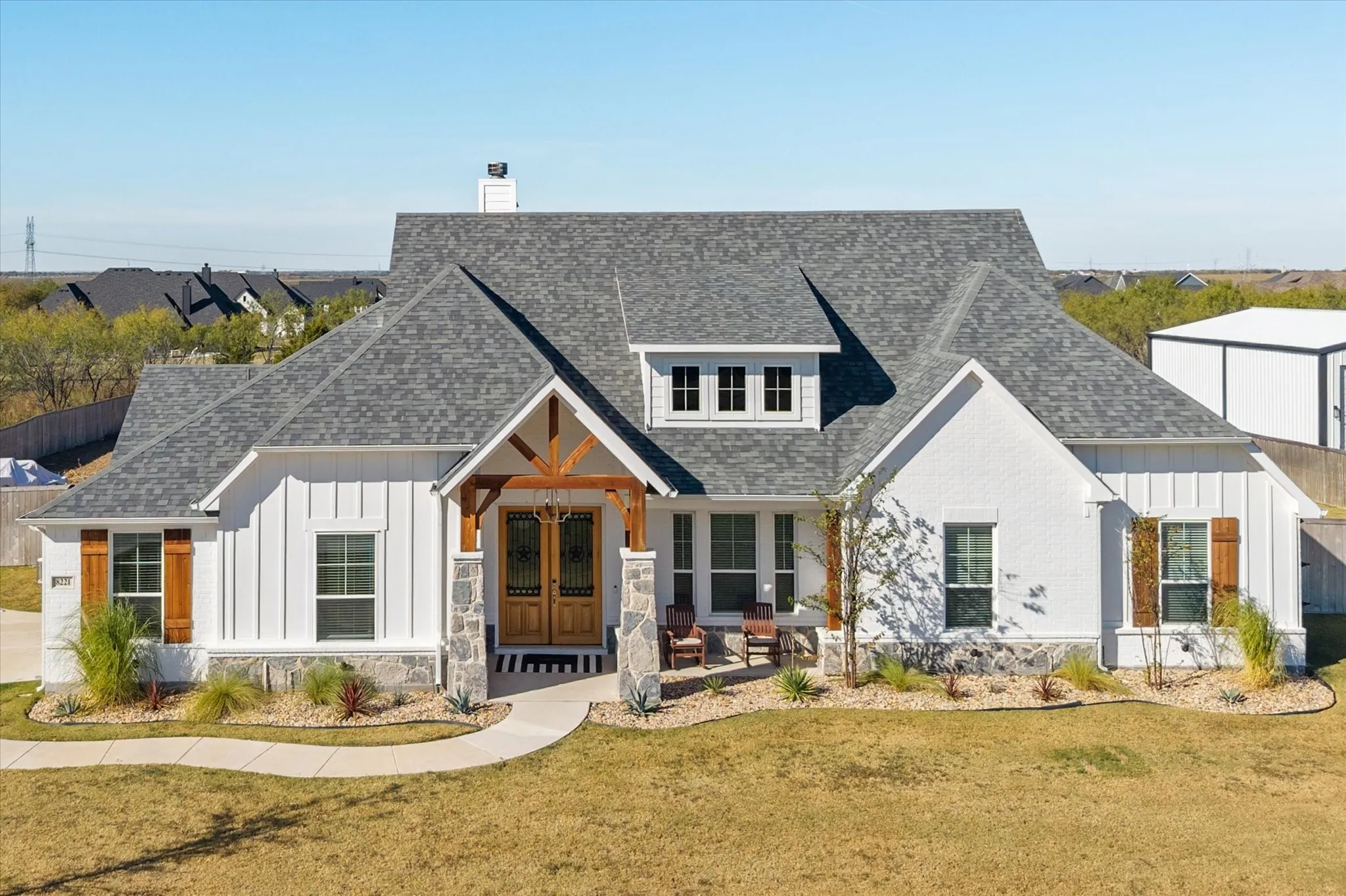 Modern farmhouse featuring board and batten siding, a shingled roof, a front lawn, a chimney, and french doors