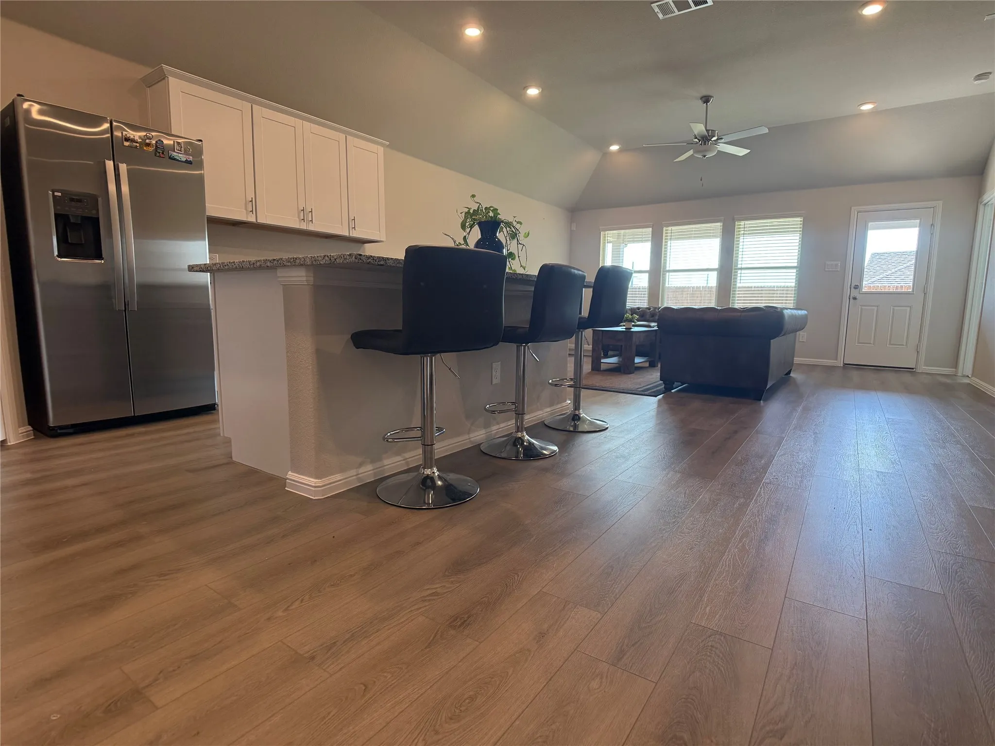 Kitchen with stainless steel fridge with ice dispenser, recessed lighting, white cabinetry, a kitchen breakfast bar, and dark wood-style flooring