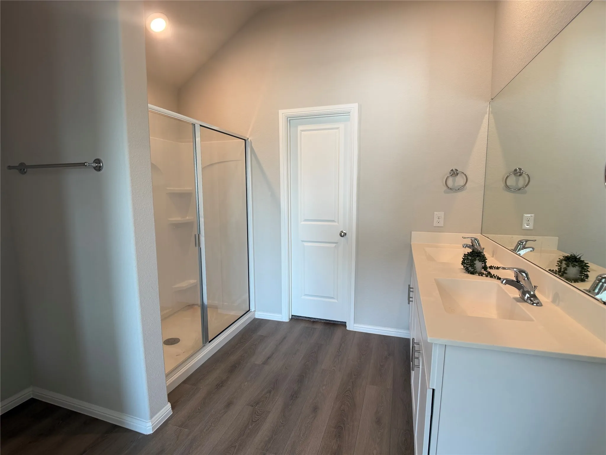 Bathroom with double vanity, dark wood-type flooring, and a shower stall