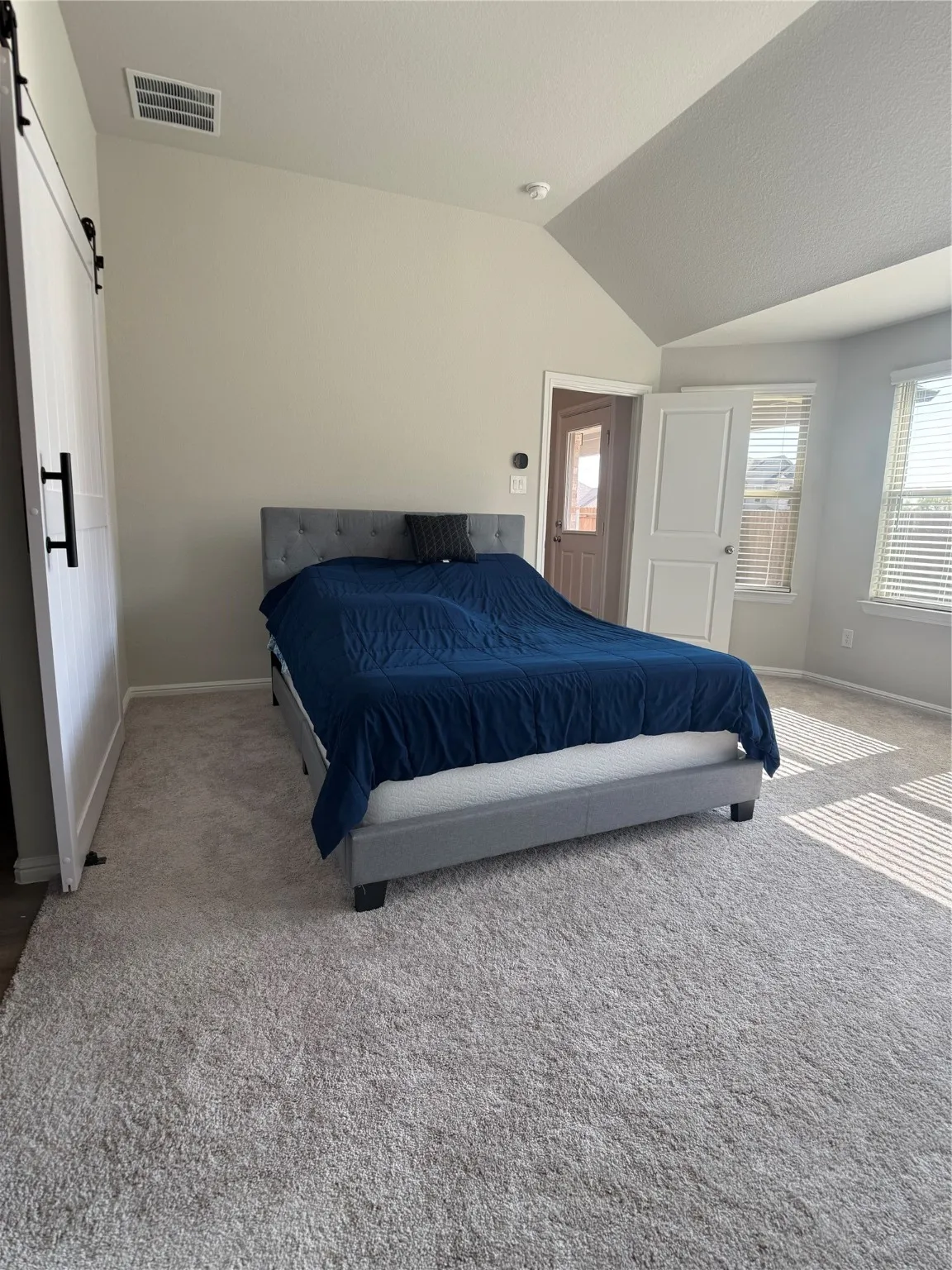Carpeted bedroom featuring a barn door and lofted ceiling
