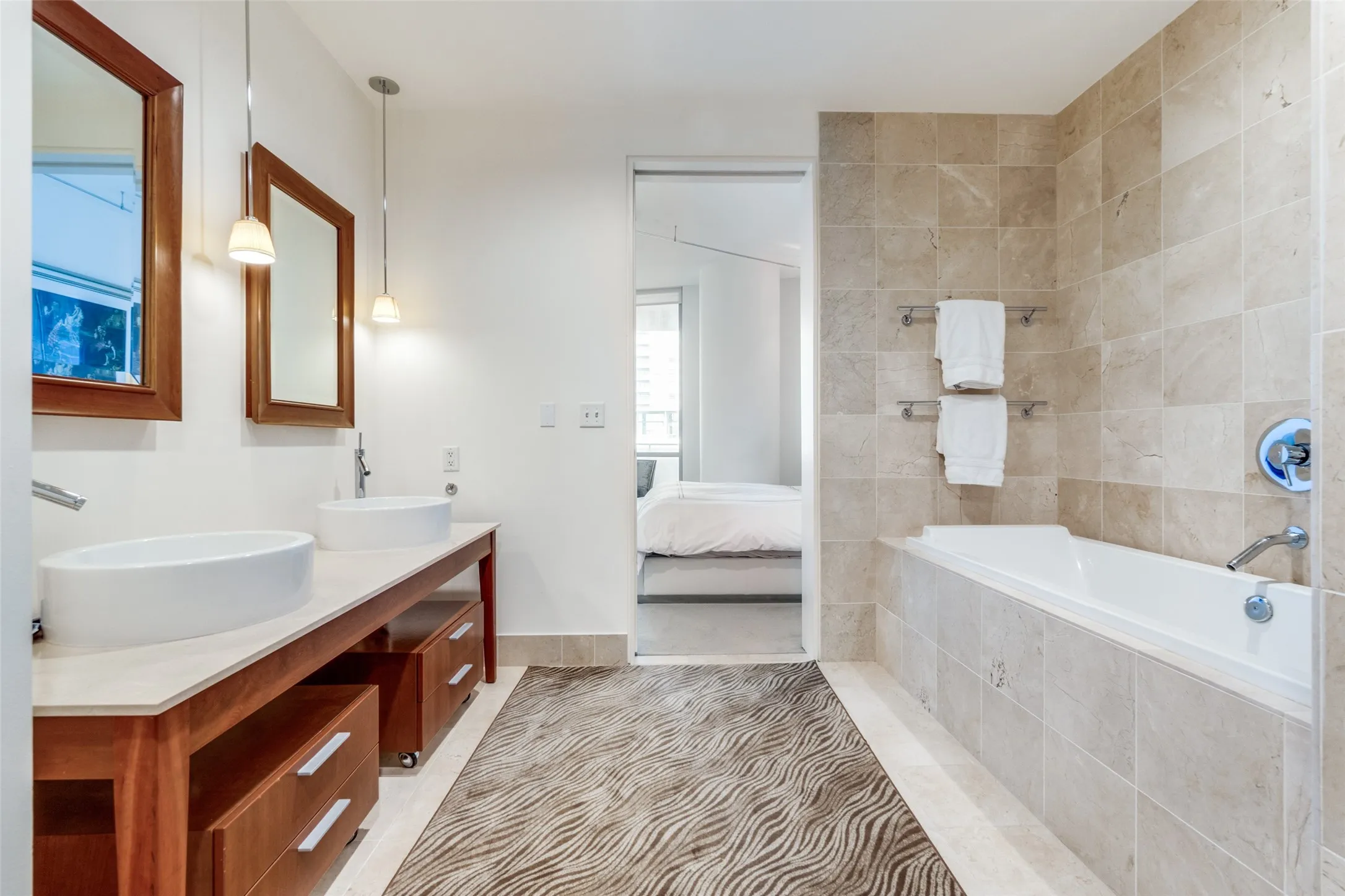 Bathroom featuring connected bathroom, light tile patterned flooring, double vanity, and a relaxing tiled tub