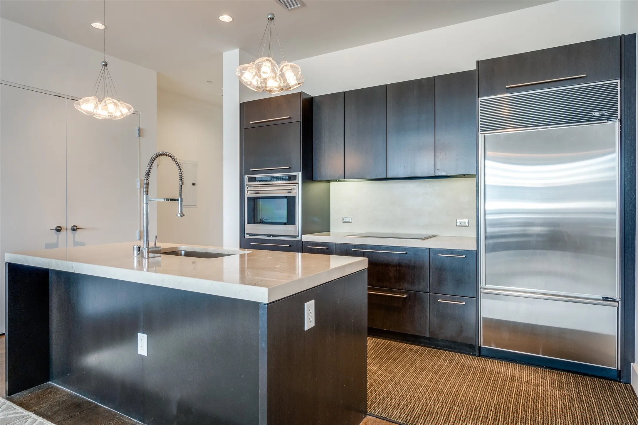 Kitchen with appliances with stainless steel finishes, decorative light fixtures, a kitchen island with sink, recessed lighting, and light stone countertops