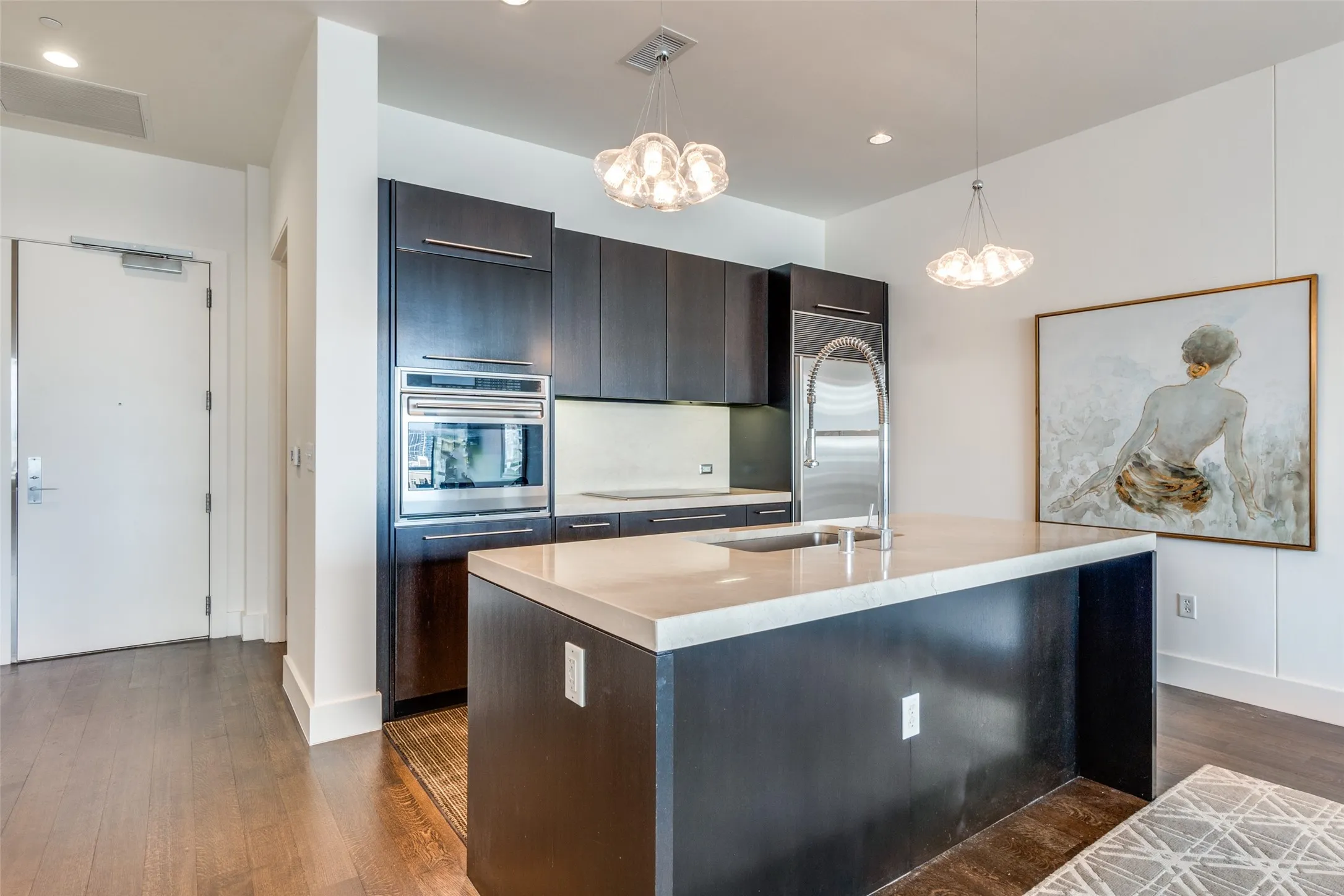 Kitchen featuring modern cabinets, hanging light fixtures, oven, dark wood finished floors, and a kitchen island with sink