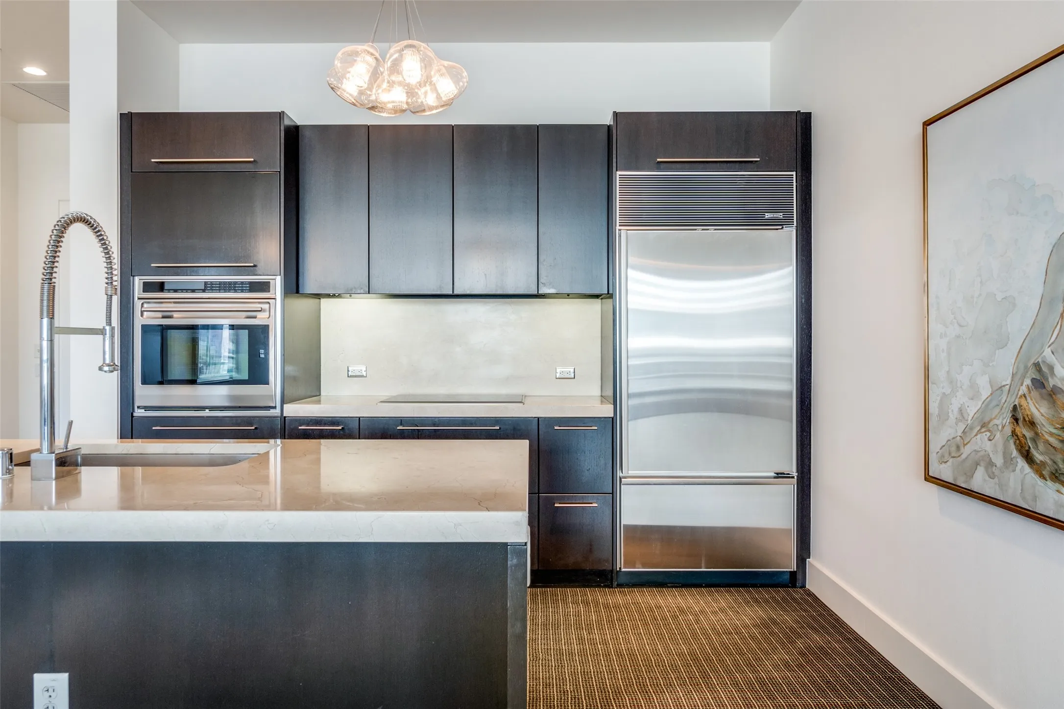 Kitchen featuring appliances with stainless steel finishes, modern cabinets, hanging light fixtures, light stone countertops, and dark brown cabinets