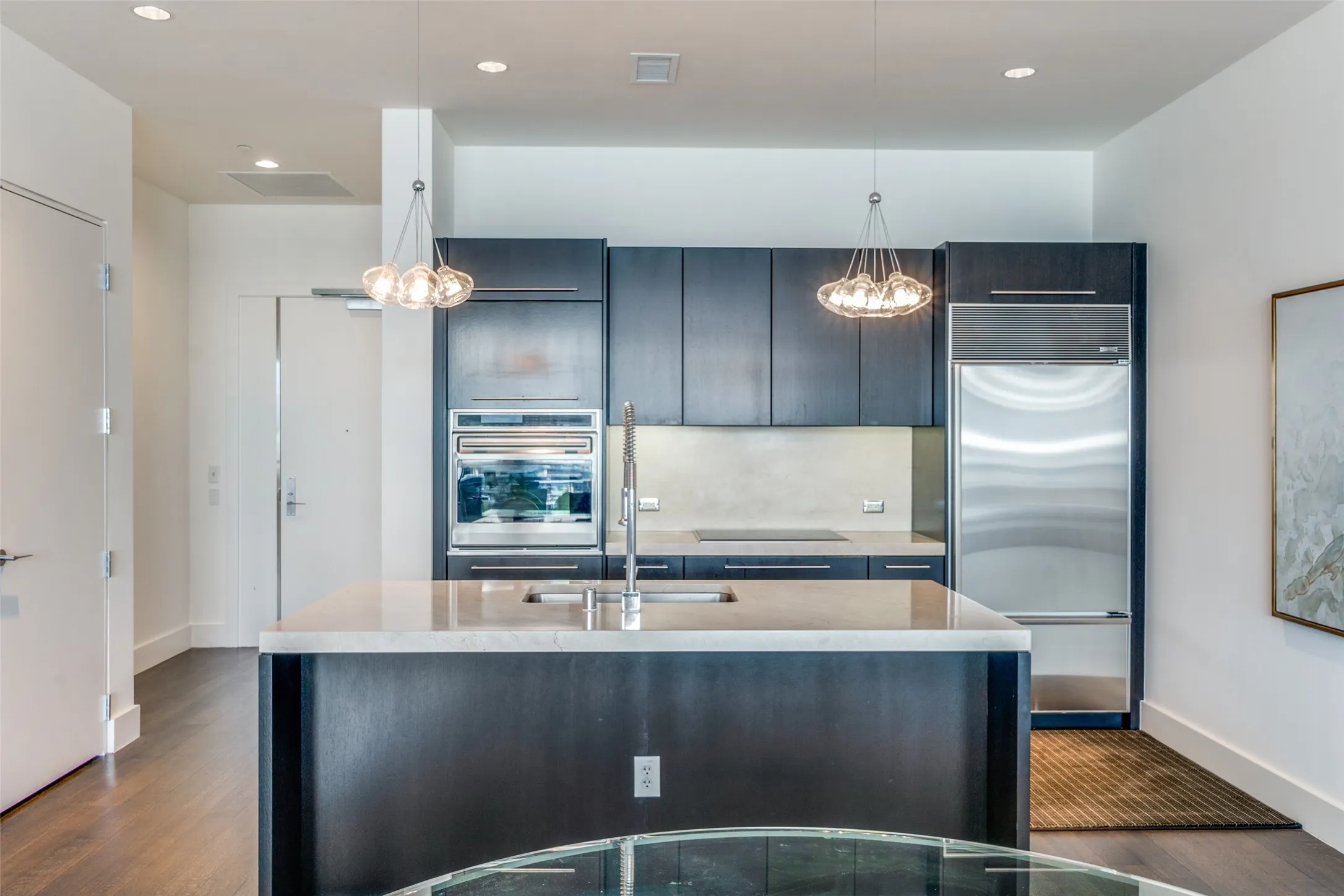 Kitchen featuring stainless steel appliances, pendant lighting, a center island with sink, dark wood-type flooring, and light stone counters