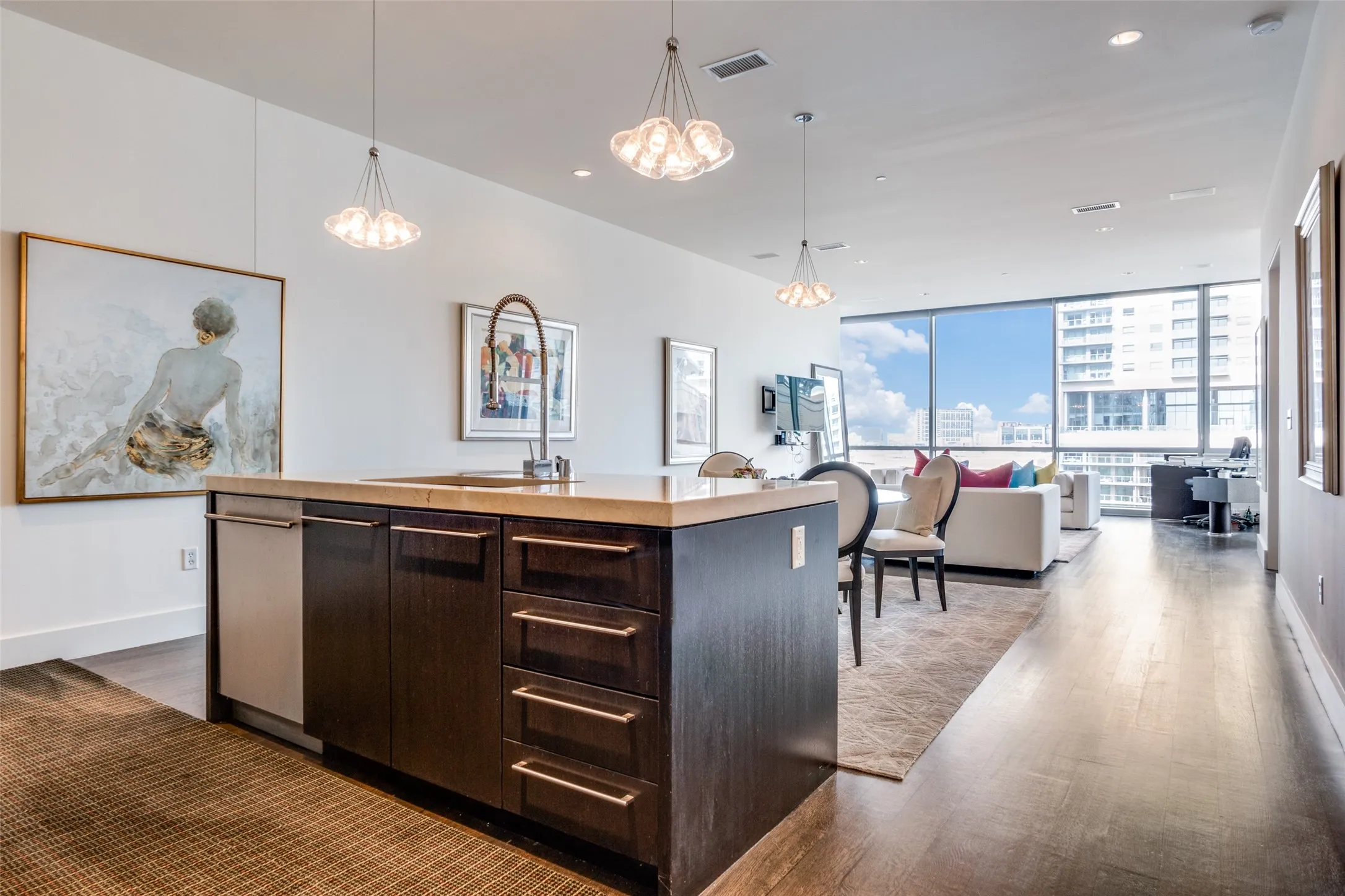Kitchen with dark brown cabinetry, hanging light fixtures, light countertops, an island with sink, and open floor plan