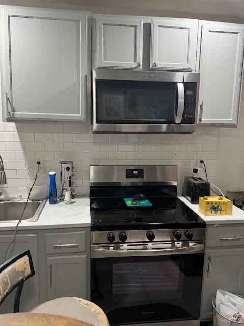Kitchen featuring stainless steel appliances, gray cabinets, light countertops, and decorative backsplash