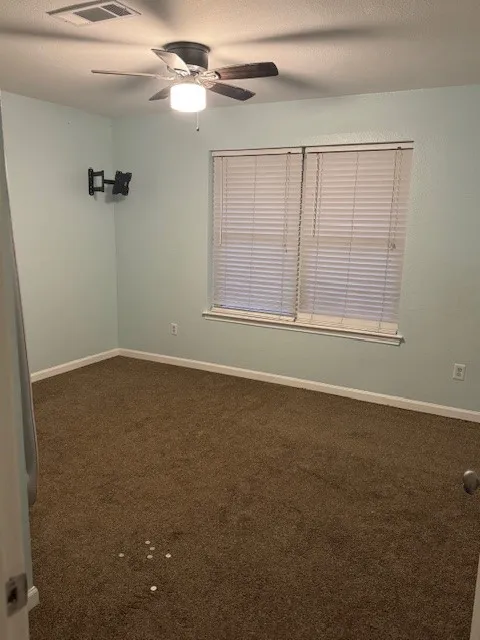 Empty room featuring dark carpet and ceiling fan