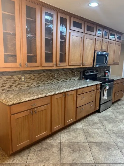 Kitchen featuring brown cabinets, appliances with stainless steel finishes, backsplash, light stone counters, and recessed lighting