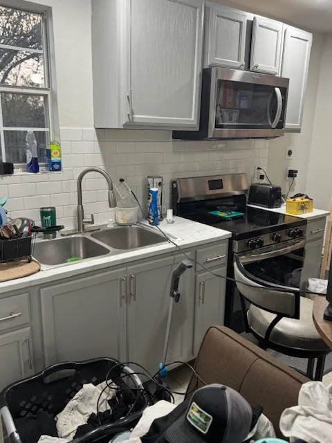 Kitchen with gray cabinetry, light countertops, appliances with stainless steel finishes, and backsplash