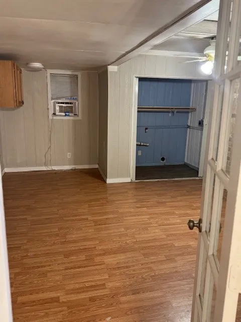 Below grade area with light wood finished floors, wooden walls, and cooling unit