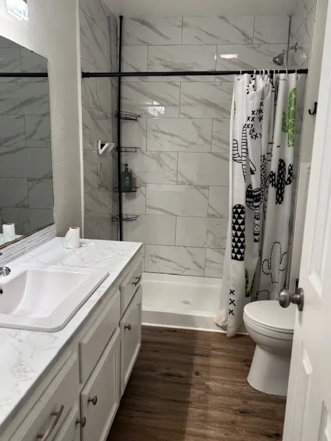Full bath with vanity, dark wood-style floors, a shower stall, and a textured wall
