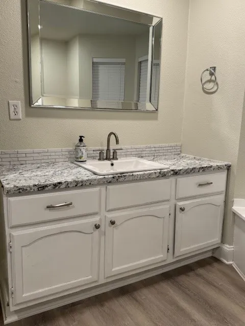 Bathroom with a textured wall, vanity, and light wood-style floors