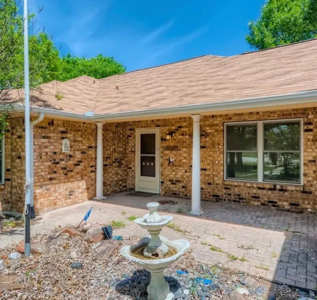 Doorway to property with roof with shingles and brick siding