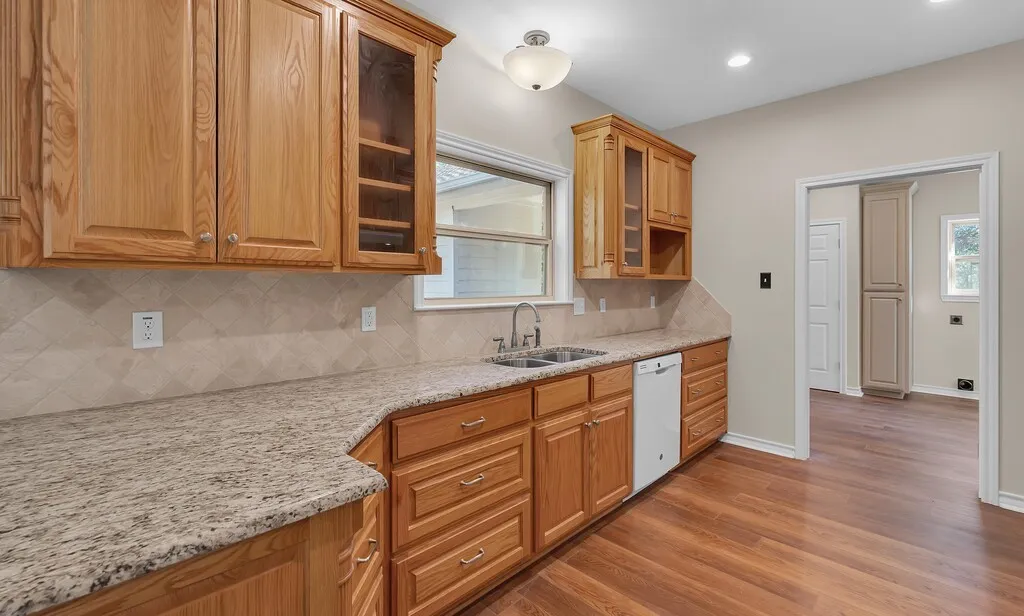 Kitchen featuring glass insert cabinets, decorative backsplash, light wood-style flooring, light stone counters, and recessed lighting