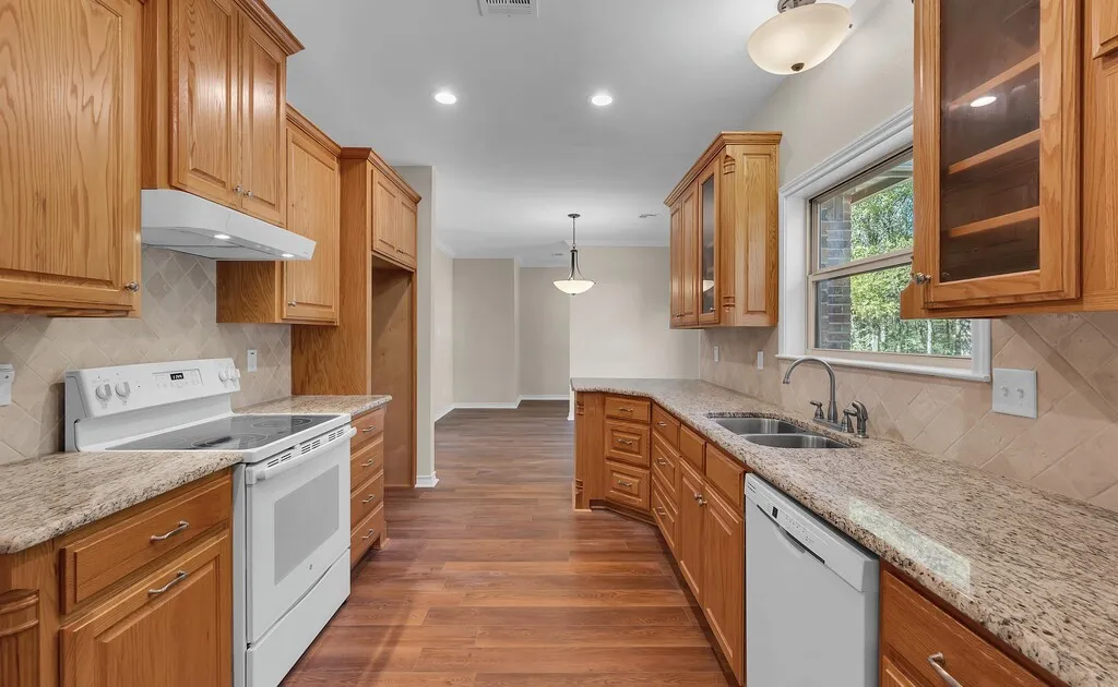 Kitchen with tasteful backsplash, decorative light fixtures, white appliances, dark wood-type flooring, and light stone countertops