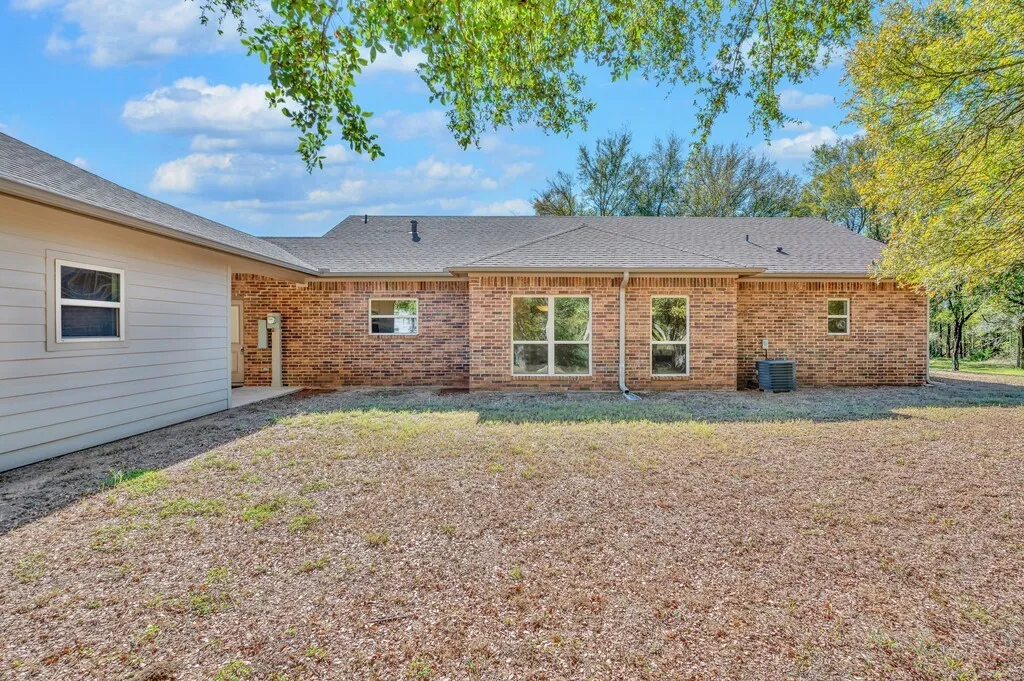 Rear view of property with a patio area, a shingled roof, brick siding, and a lawn