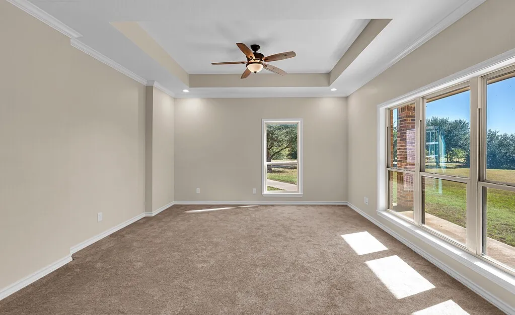 Empty room with a raised ceiling, ornamental molding, light carpet, and ceiling fan