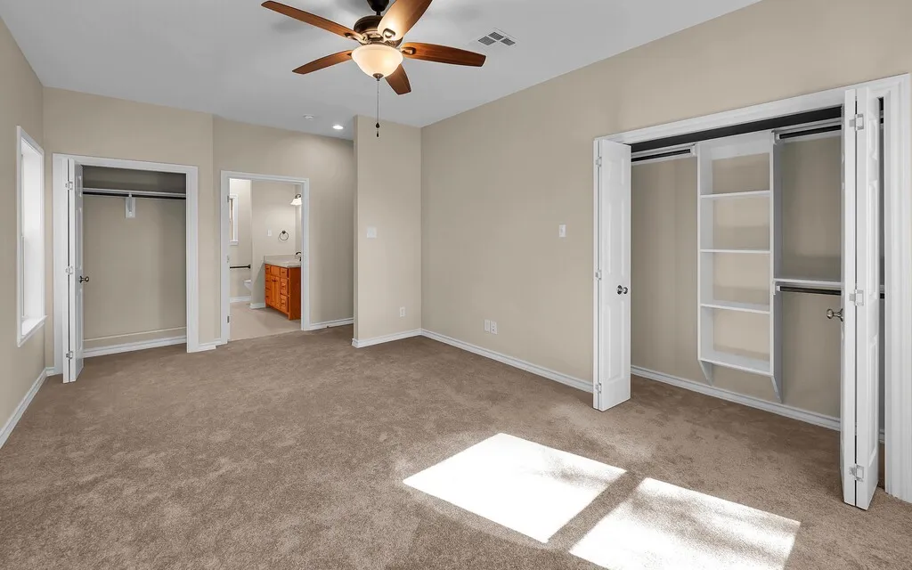 Unfurnished bedroom with a closet, light colored carpet, a ceiling fan, and ensuite bath