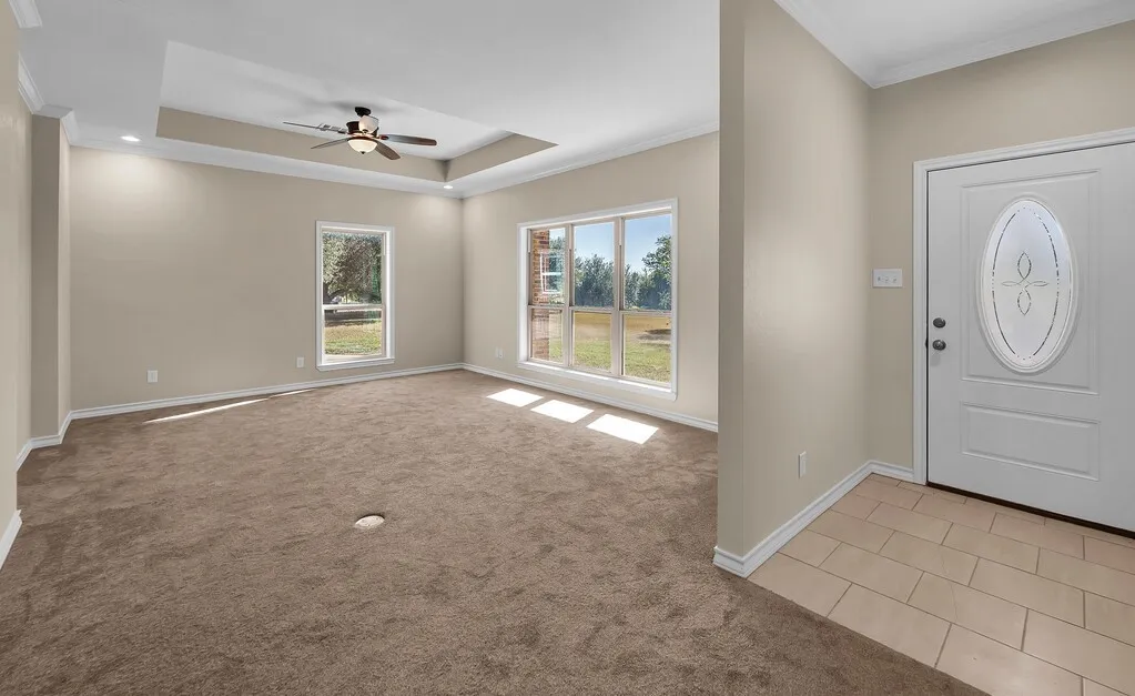 Entrance foyer featuring crown molding, a raised ceiling, light carpet, light tile patterned floors, and ceiling fan